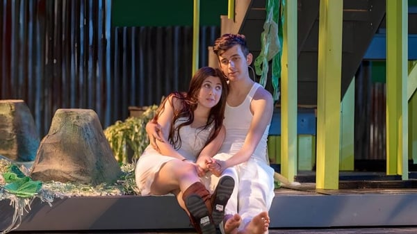 Zwei Schülerinnen sitzen zusammen auf einer Bank im Außenbereich der Calabasas High School vor bunten Gebäuden und Bepflanzung.