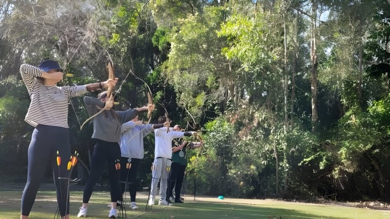 Schüler des Calamvale Community College üben Bogenschießen im Freien inmitten grüner Umgebung.
