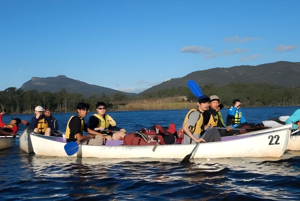 Schüler des Calamvale Community College unternehmen eine Bootsfahrt auf einem Bergsee bei blauem Himmel.