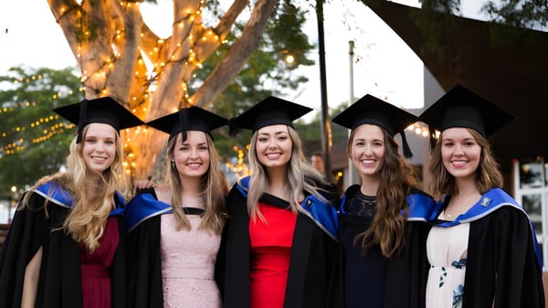 Fünf Schülerinnen stehen in ihren Abschlussroben zusammen vor einem Baum auf dem Campus des Calamvale Community College.