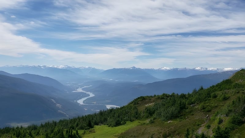 Eine grüne Berglandschaft mit einem Fluss und schneebedeckten Gipfeln im Hintergrund nahe der Caledonia Secondary School.