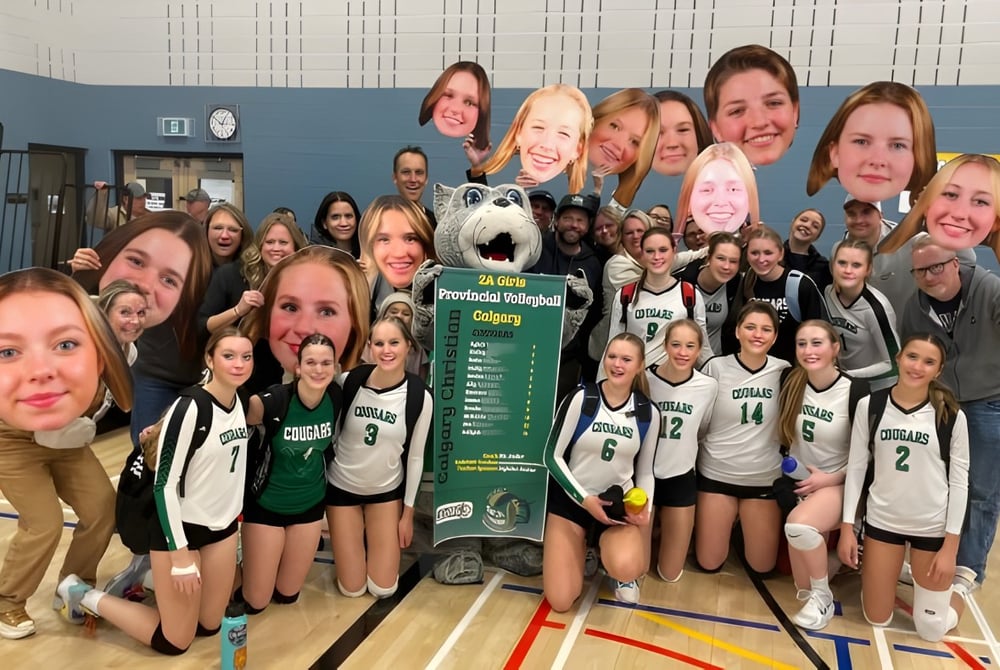 Eine Gruppe junger Basketballspielerinnen posiert in der Turnhalle vor einem großen Banner auf dem Calgary Christian School steht.