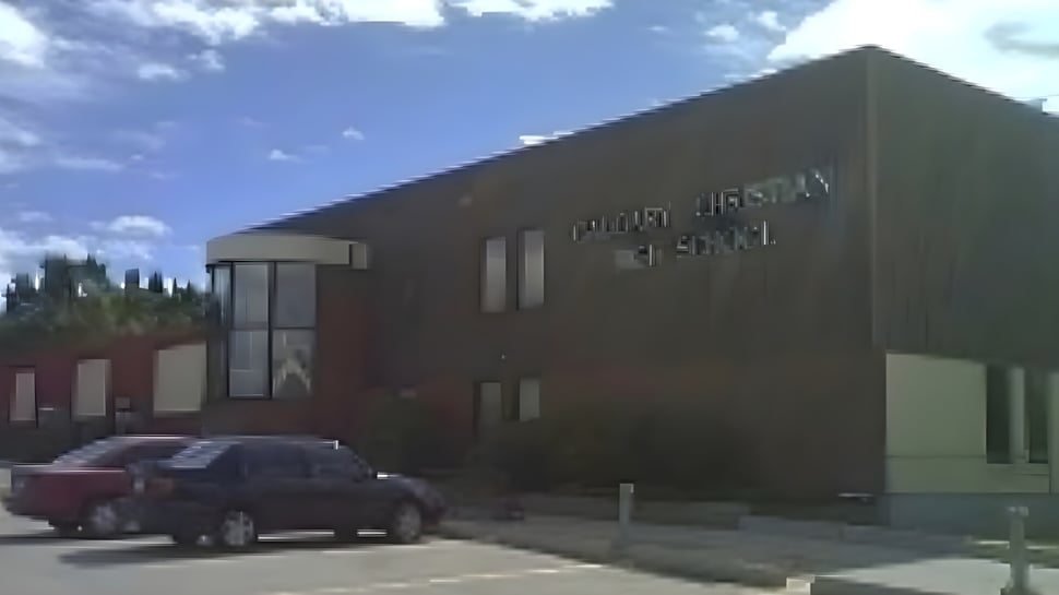 Das große Gebäude der Calgary Christian School mit dem Schriftzug und einem roten Fahrzeug im Vordergrund unter bewölktem Himmel.