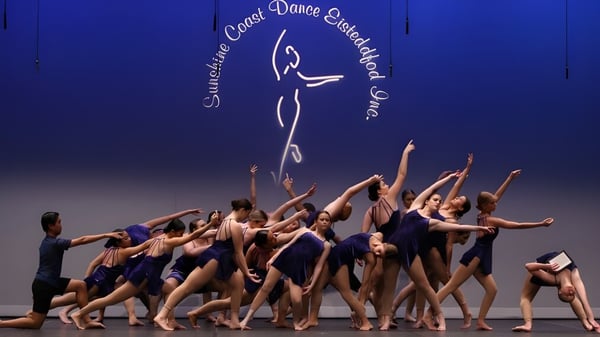 Eine Gruppe von Tänzern führt auf der Bühne vor großem Logo der Sunshine Coast Dance Company an der Caloundra State High School auf.