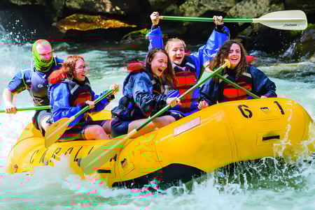Schüler der Caloundra State High School fahren mit einem gelben Schlauchboot auf einem Fluss durch grünes Vegetationsgebiet.