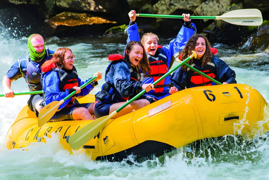 Schüler der Caloundra State High School fahren mit einem gelben Schlauchboot auf einem Fluss durch grünes Vegetationsgebiet.