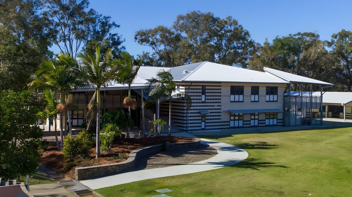 Das zweistöckige Holzgebäude mit Metalldach von Caloundra State High School ist von üppigem Grün und Palmen umgeben.