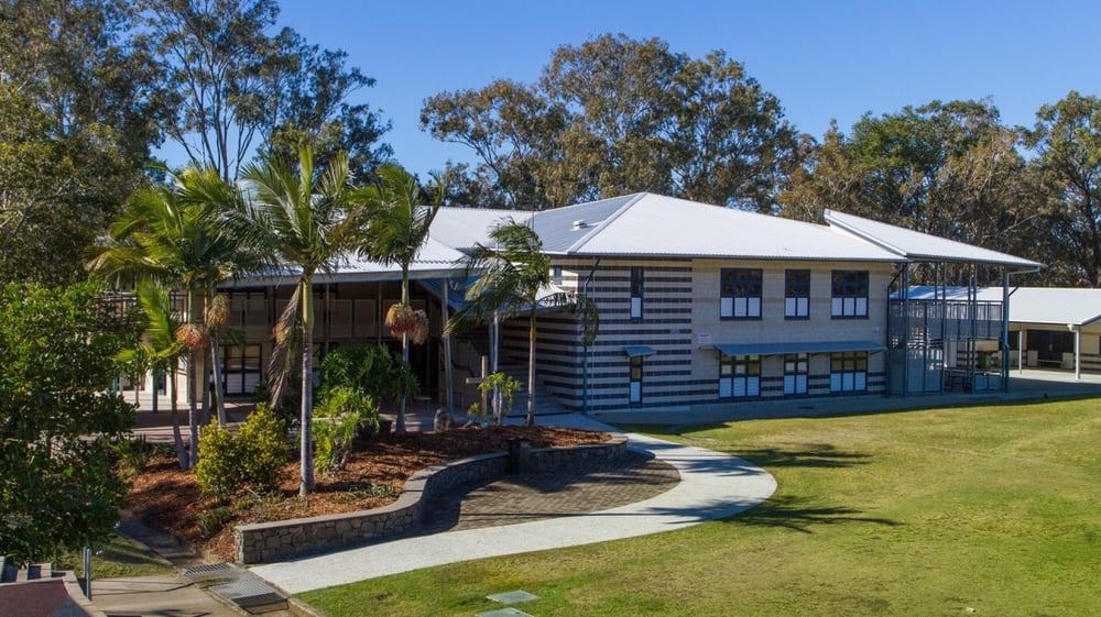 Das zweistöckige blaue Holzgebäude mit weißem Dach auf dem Campus der Caloundra State High School ist von Palmen und gepflegtem Rasen umgeben.