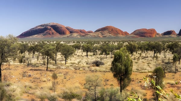 Das Bild zeigt eine weite Wüstenlandschaft mit roten Felsen und vereinzelter Vegetation vor dem Hintergrund der Caloundra State High School.