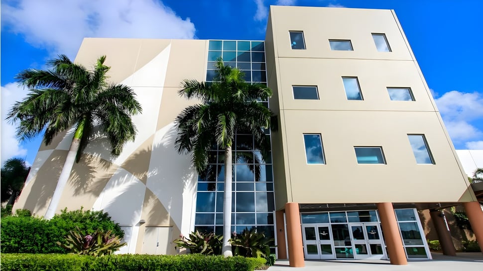 Das mehrstöckige Gebäude der Calvary Christian Academy ist von tropischen Palmen umgeben und steht unter klarem blauem Himmel.