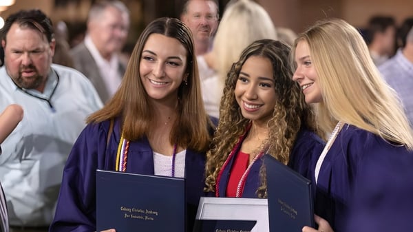 Drei Schülerinnen in Abschlusskleidung halten stolz ihre Diplome bei der Abschlussfeier der Calvary Christian Academy.