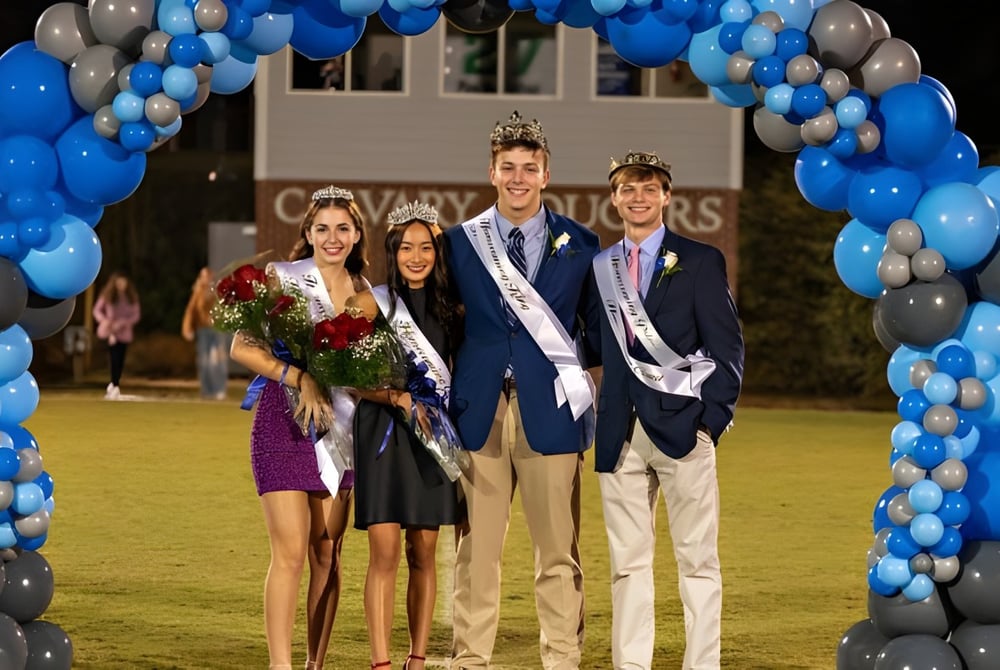 Eine Gruppe von vier Personen steht vor einem Ballonbogen auf dem Campus der Calvary Day School.