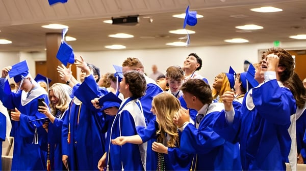 Eine Gruppe von Absolventen in blauen Talaren feiert ihren Abschluss im geschmückten Innenraum der Calvary Day School.