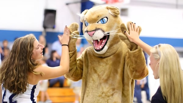 Eine Schülerin der The Calverton School interagiert mit dem großen Maskottchen in der Sporthalle.