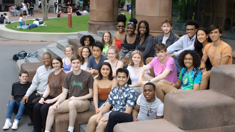 Eine Gruppe von Schülerinnen und Schülern der Cambridge Rindge and Latin High School versammelt sich im Außenbereich mit Gebäuden und Grünflächen im Hintergrund.