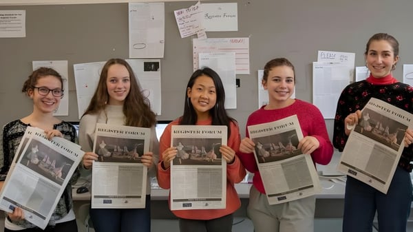 Fünf Schülerinnen der Cambridge Rindge and Latin High School stehen mit Zeitungen in einem Klassenraum.