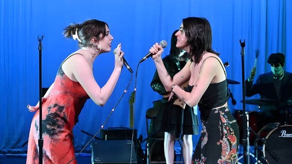 Zwei Schülerinnen führen auf der Bühne der The Cambridge School of Weston vor blauem Hintergrund mit Musikinstrumenten auf.