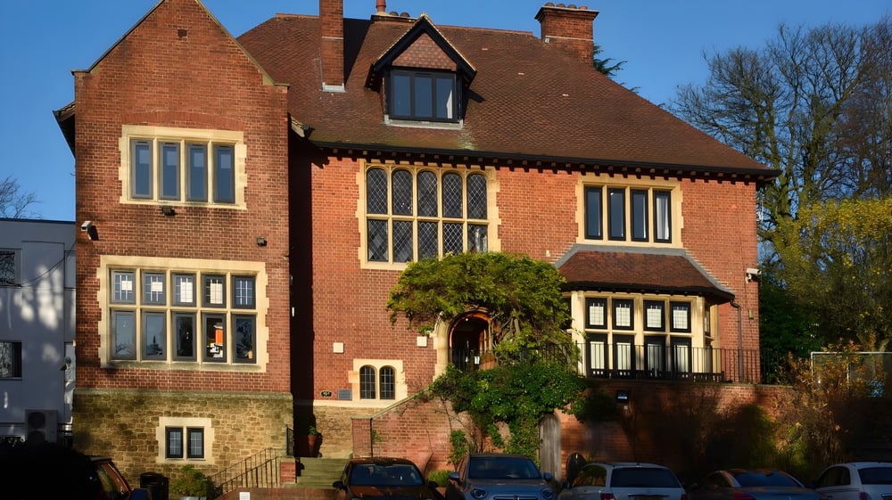 Das Hauptgebäude des Cambridge Tutors College ist ein großes, verziertes Backsteingebäude mit einem steilen Dach und umgeben von Bäumen.