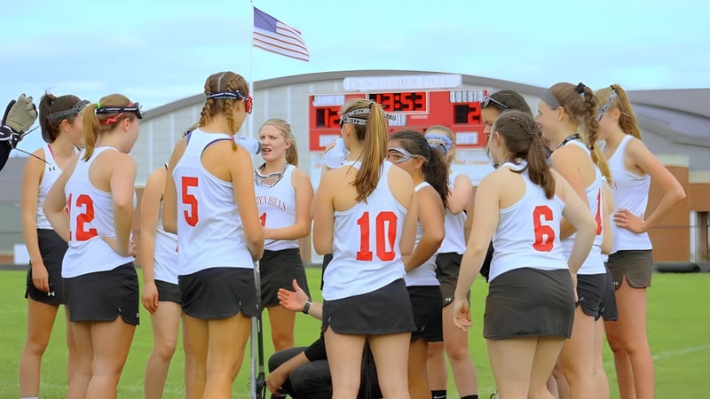 Eine Gruppe junger Athletinnen steht auf dem Sportfeld der Camden Hills Regional High School mit einer amerikanischen Flagge im Hintergrund.