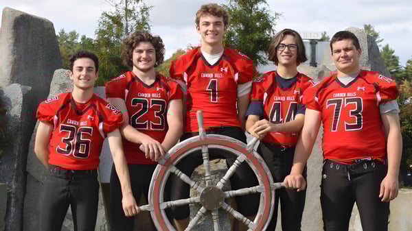 Eine Gruppe Schüler der Camden Hills Regional High School posiert in roten Sportuniformen vor einer natürlichen Kulisse mit Bäumen und bewölktem Himmel.