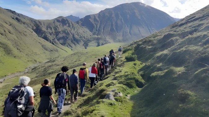 Eine Gruppe von Schülern des Campus La salle Saint Christophe wandert auf einem grünen Bergpfad umgeben von hohen Gipfeln.