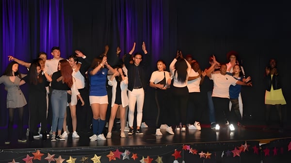 Eine Gruppe von Schülerinnen und Schülern steht auf der Bühne des Campus La Salle Saint Christophe mit erhobenen Armen vor dunklem Vorhang und bunter Beleuchtung.