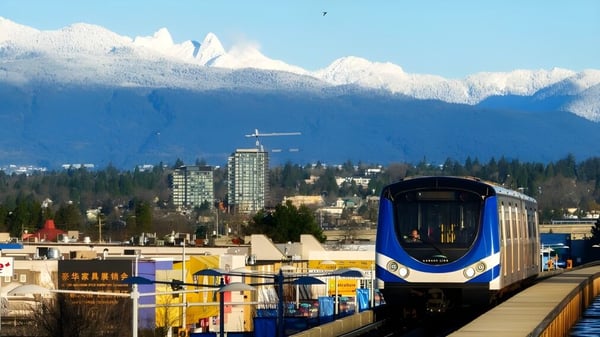 Eine moderne Stadtbahn fährt vor schneebedeckten Bergen in der Nähe der Canada Star Secondary School.