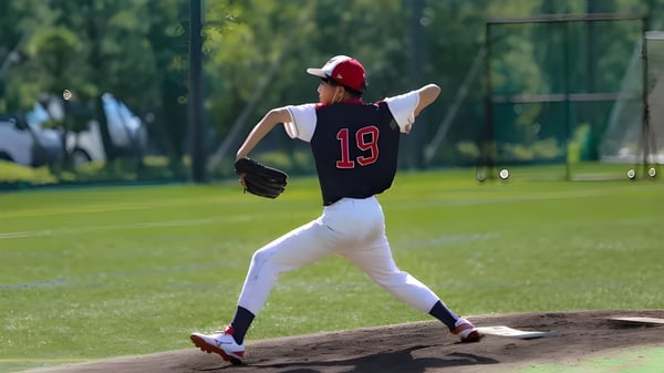 Eine junge Baseballspielerin in roter und schwarzer Uniform steht auf dem Wurfhügel auf dem Sportplatz der Canadian Academy.
