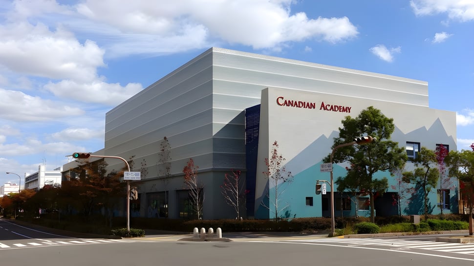 Das moderne Hauptgebäude der Canadian Academy ist von Bäumen umgeben und befindet sich an einem Zebrastreifen.