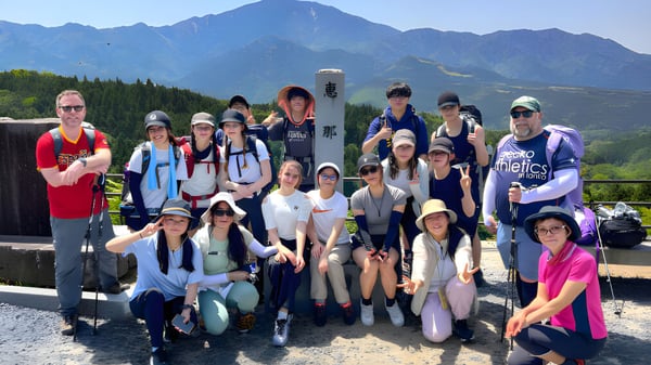 Eine Gruppe junger Menschen posiert vor dem Bergpanorama auf dem Campus der Canadian Academy.