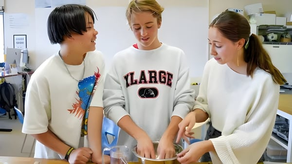Drei Schülerinnen und Schüler der Canadian Academy stehen gemeinsam in einer Küche oder einem Labor und diskutieren eine Aufgabe.