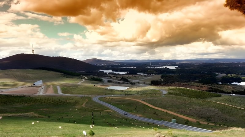 Landschaft mit Hügeln und einer Stadt im Hintergrund unter wolkigem Himmel nahe dem Canberra College.