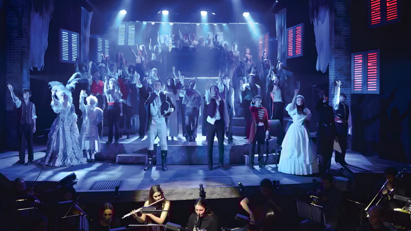 Eine große Gruppe von Schülerinnen und Schülern der Canford School steht in formeller Kleidung auf der Bühne während einer Aufführung.