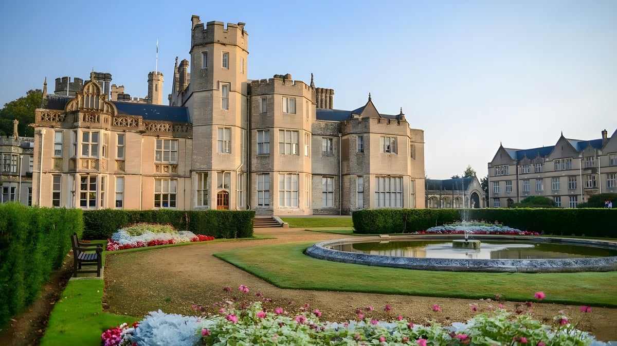 Das Schloss der Canford School steht umgeben von einem gepflegten Garten mit Brunnen und Blumenbeeten.