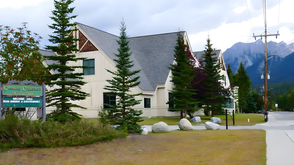 Das rustikale Gebäude der Canmore Collegiate High School steht eingebettet in eine bewaldete Landschaft mit hohen Kiefern und Bergen im Hintergrund.