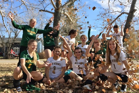 Eine Gruppe von Schülern der Canmore Collegiate High School versammelt sich in einem Park mit herbstlichen Blättern unter blauem Himmel.