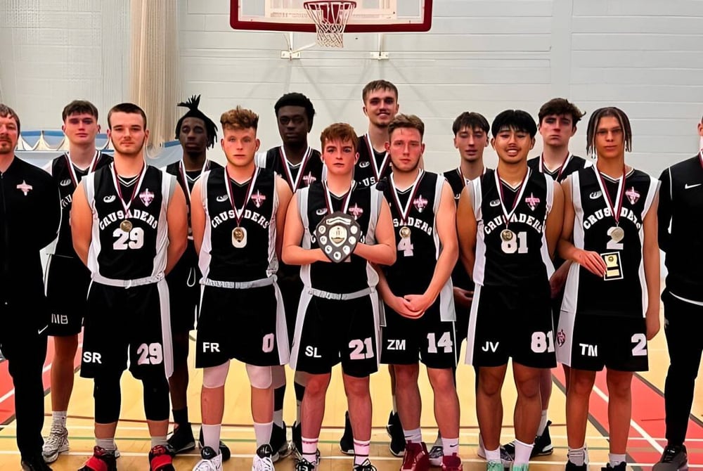 Eine Gruppe von Schülerinnen und Schülern der Canterbury Academy posiert gemeinsam in der Turnhalle vor einem Basketballkorb.