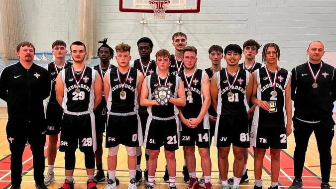 Eine Gruppe von Schülerinnen und Schülern der Canterbury Academy posiert in der Turnhalle vor einem Basketballkorb.