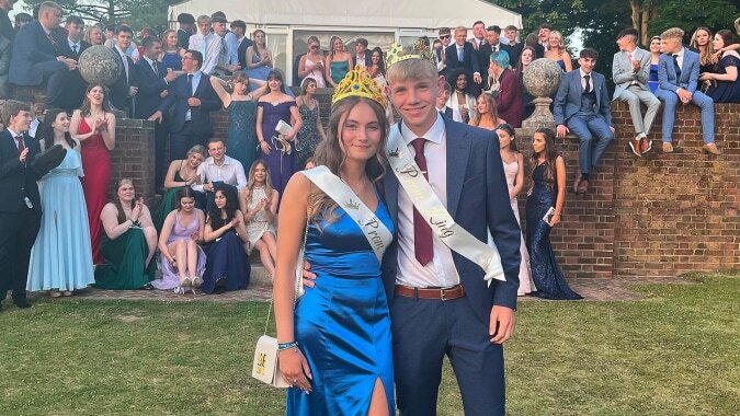 Eine Gruppe in formeller Kleidung steht vor einer Menschenmenge auf einer Wiese auf dem Gelände der Canterbury Academy.