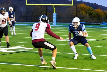 Zwei Football-Spieler laufen auf dem Spielfeld der Canterbury School mit herbstlichem Laub im Hintergrund.
