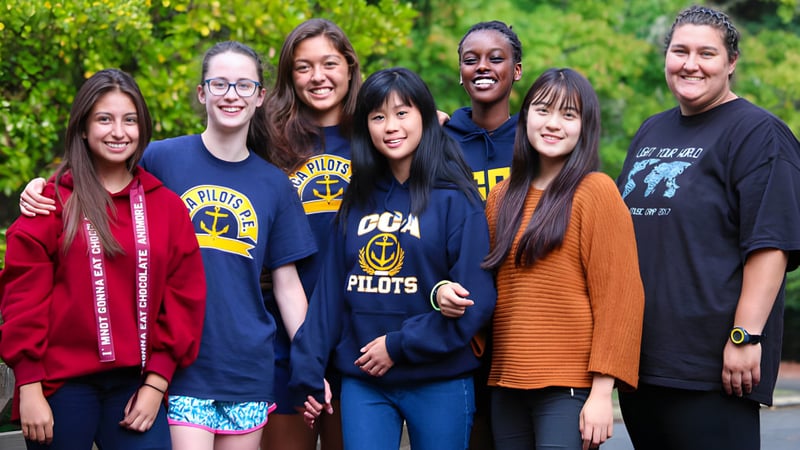 Eine Gruppe Schülerinnen und Schüler steht lächelnd in einer grünen Außenanlage der Canyonville Academy.