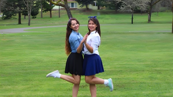 Zwei Schülerinnen der Canyonville Academy stehen zusammen und lächeln in einem Park mit Gras und Bäumen.