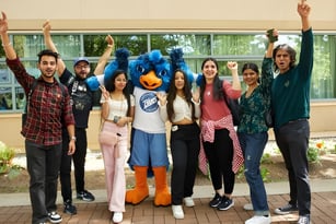 Eine Gruppe junger Menschen steht mit erhobenen Armen vor einem Gebäude auf dem Campus der Capilano University.