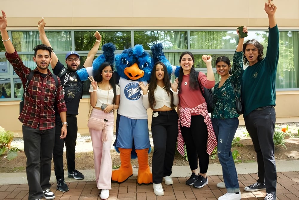 Eine Gruppe junger Menschen steht mit erhobenen Armen vor einem Gebäude auf dem Campus der Capilano University.