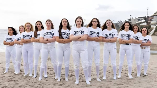Eine Gruppe von Schülerinnen in weißen Uniformen mit Eagles-Schriftzug steht am Strand bei bewölktem Himmel auf dem Campus der Capistrano Valley Christian.