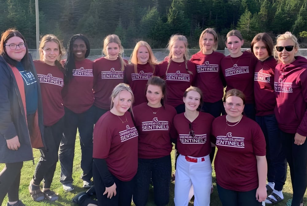 Eine Gruppe Schülerinnen der Carbonear Collegiate High School steht auf einem Grasfeld umgeben von Bäumen.