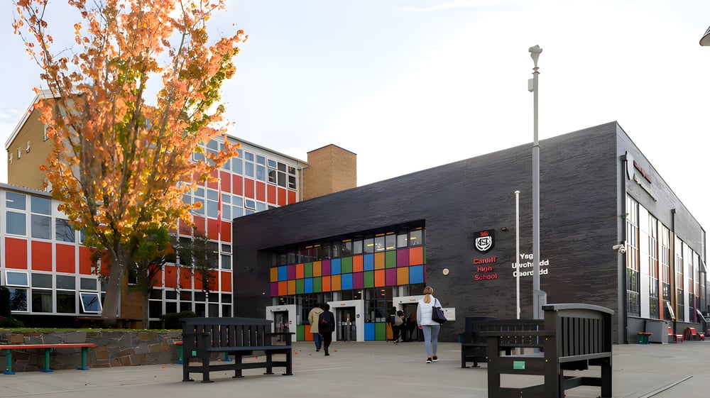 Das bunte und moderne Gebäude der Cardiff High School mit einem herbstlichen Baum im Vordergrund und Personen auf dem Schulgelände.