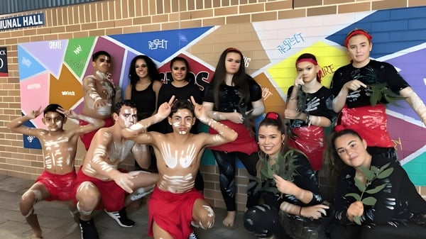 Eine Gruppe von Schülerinnen und Schülern der Cardiff High School steht vor einem bunten Wandbild an einer Backsteinmauer.