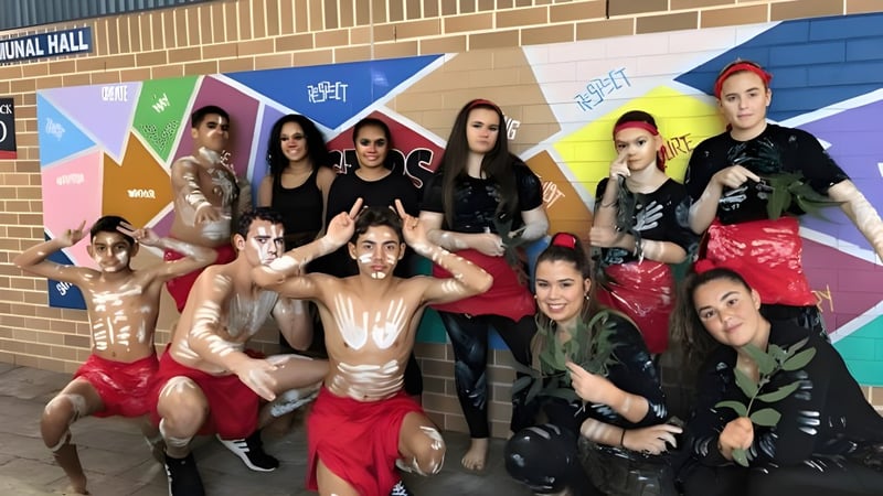 Eine Gruppe von Schülerinnen und Schülern der Cardiff High School steht vor einem bunten Wandbild an einer Backsteinmauer.