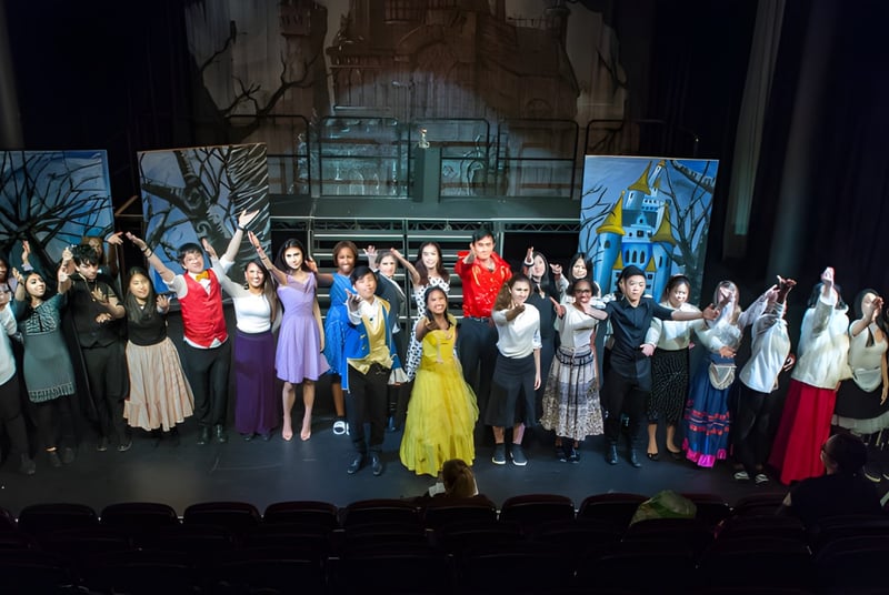 Eine Gruppe von Schülerinnen und Schülern des Cardiff Sixth Form College tritt in farbenfrohen Kostümen auf einer Bühne vor einer Waldkulisse auf.